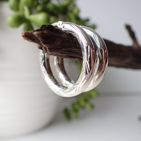 sterling silver open etched design hoop earrings hanging on driftwood