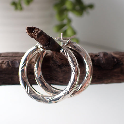 sterling silver open etched design hoop earrings hanging on driftwood